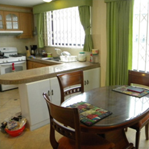 Dining area showing a wooden table, green curtains and kitchen in the background